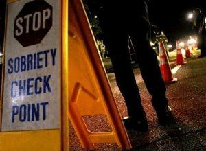 A Sign reading "Sobriety Check Point" with a police officer standing beside it.
