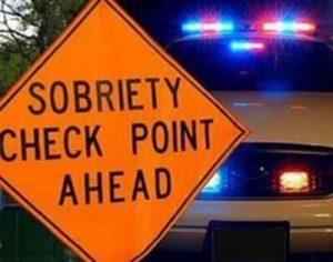 An orange sign with text: "Sobriety Check Point Ahead" with flashing police lights in the background, emphasizing finding DUI checkpoints